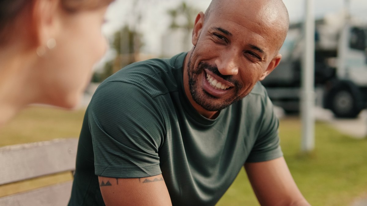 A man in a green shirt smiling outdoors.