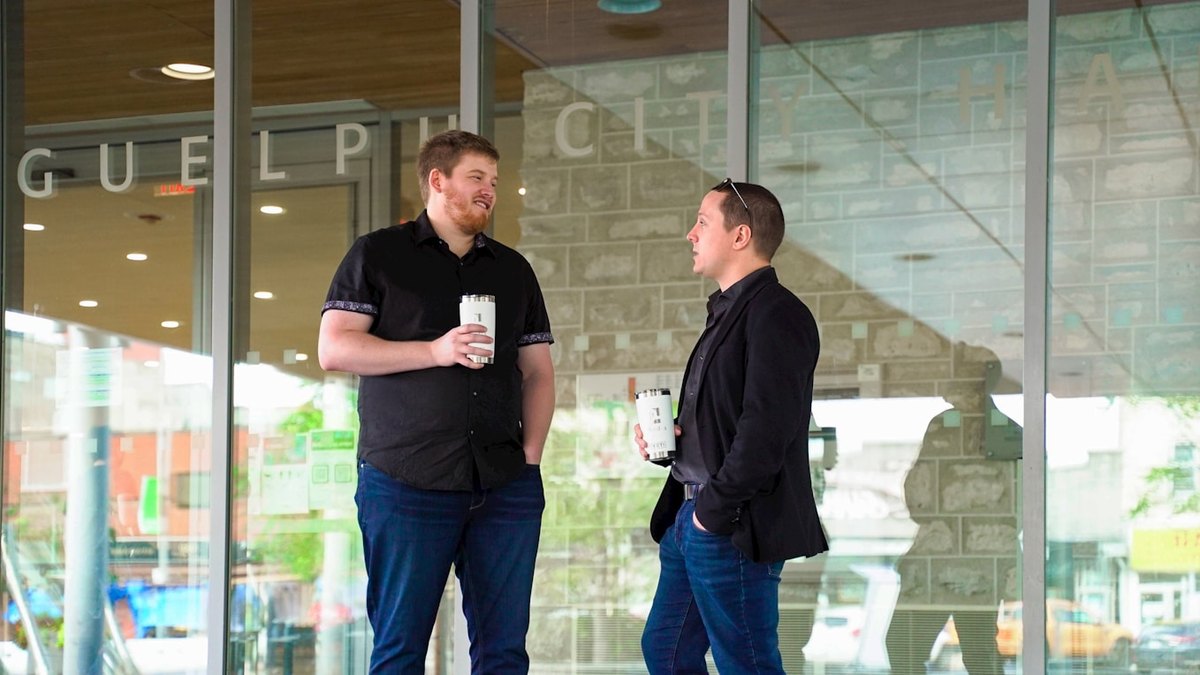 Two men talking over coffee outside a city building.