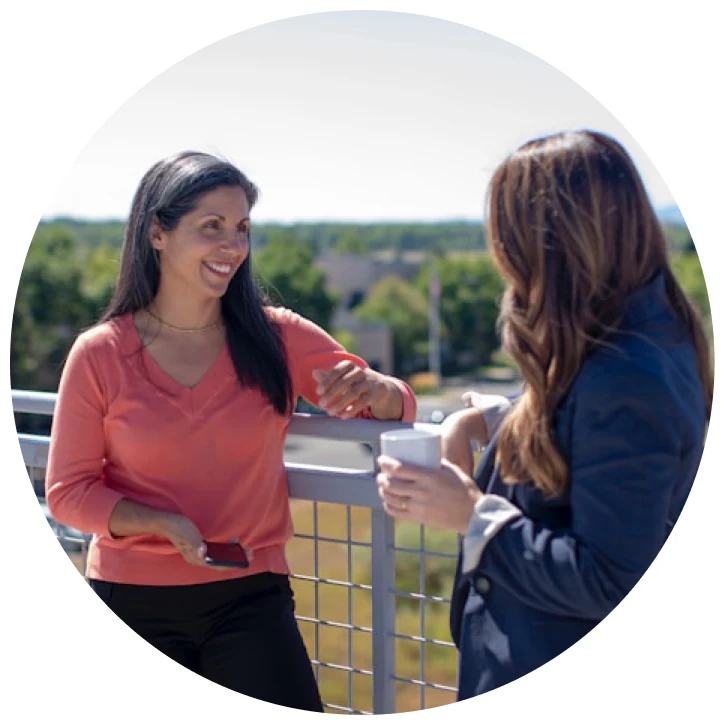 Two women talking outdoors on a balcony.