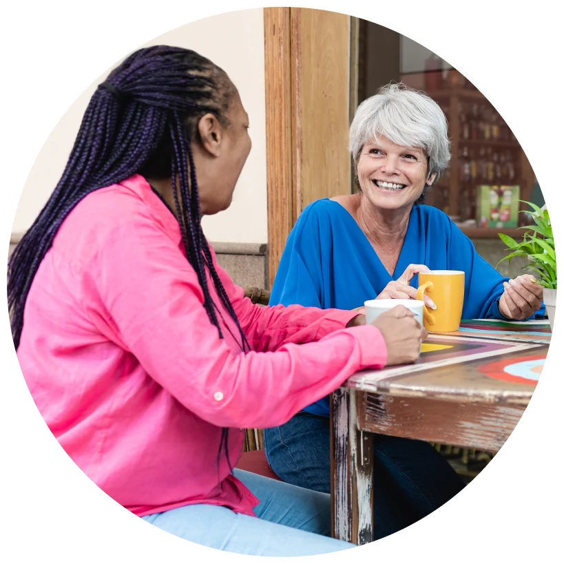 Two women talking across a table with mugs.